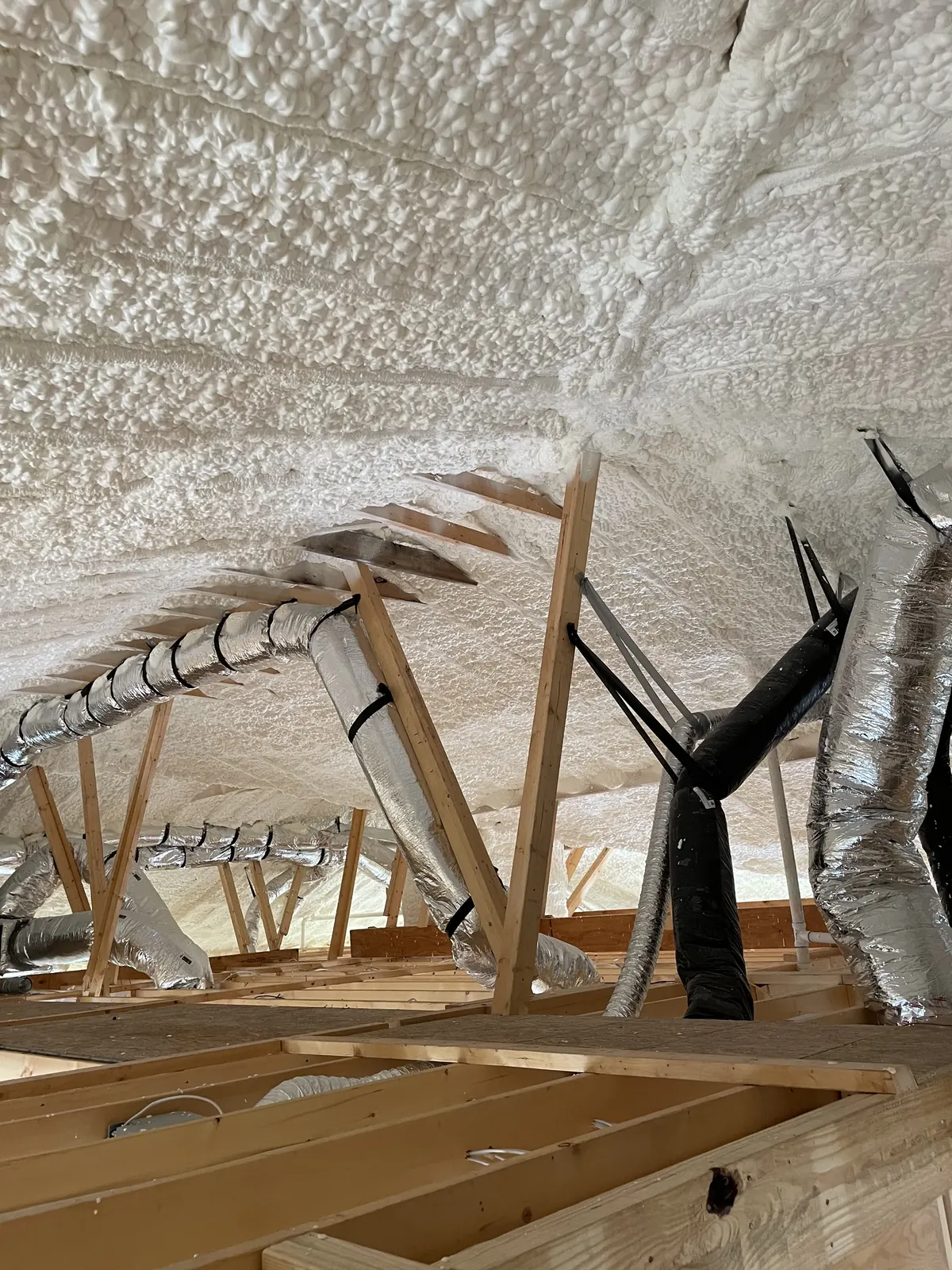 Spray foam covering an attic roof deck between the rafters, with insulated ducting running through the space