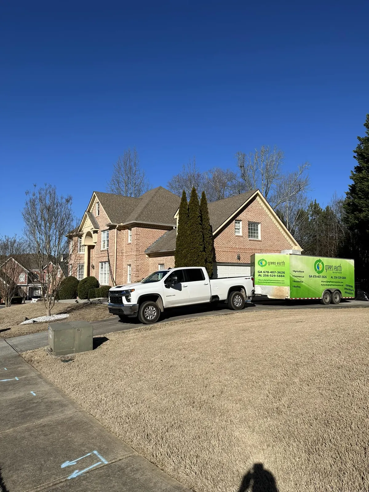 Green Earth Spray Foam truck and trailer parked on the driveway of a brick home before a residential job