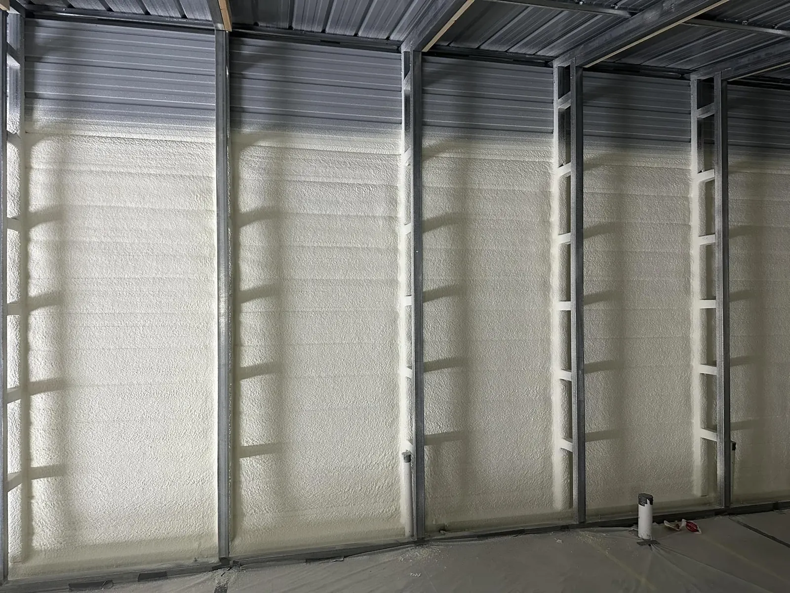 Interior of a metal building with spray foam insulation applied across the wall panels between the framing